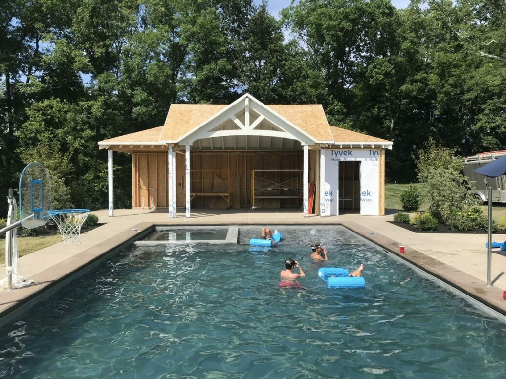 pool house framing with pool out front and people swimming