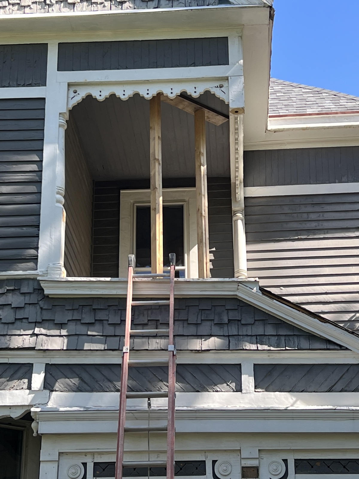 A ladder leaning against a Victorian home up to the balcony