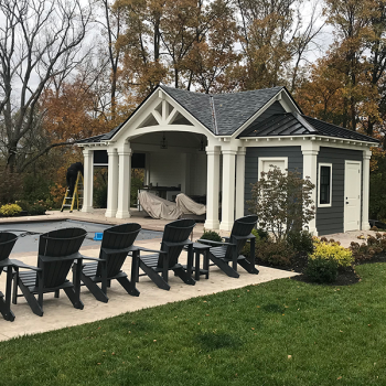 a pool house with chairs sitting on the edge of a pool